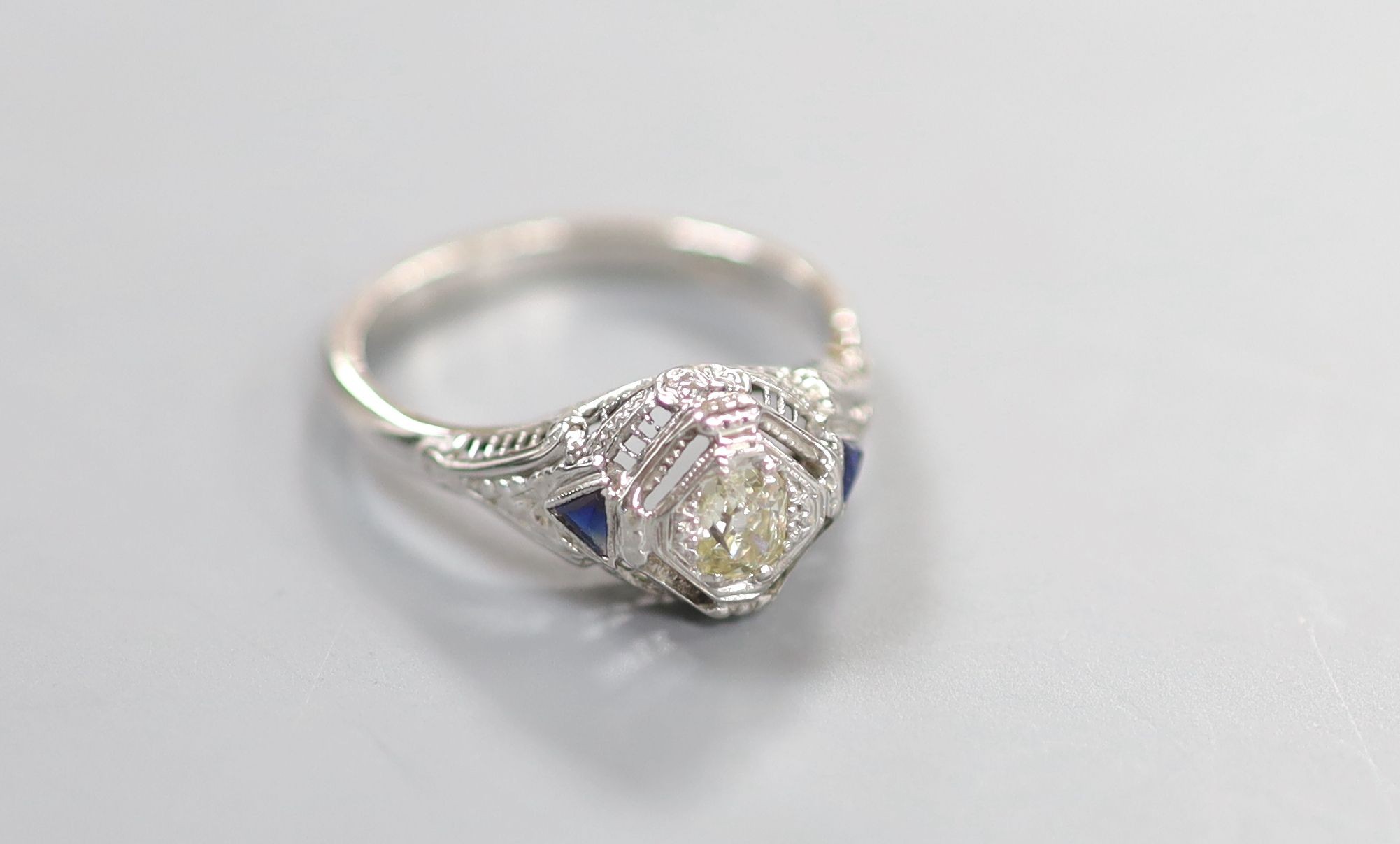 A 18ct white metal and single stone diamond ring, with triangular cut blue stone set shoulders, size P, gross weight 3.2 grams.